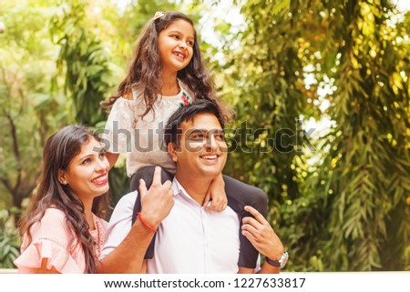 Beautiful Indian family enjoying in a park. Little girl sitting on her father's shoulders.