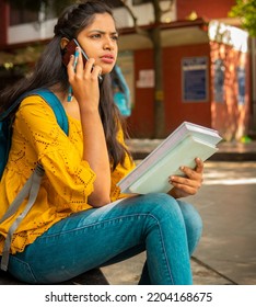Beautiful Indian Female College Student Holding Books And Busy In Talking On Mobile Phone At Campus. 