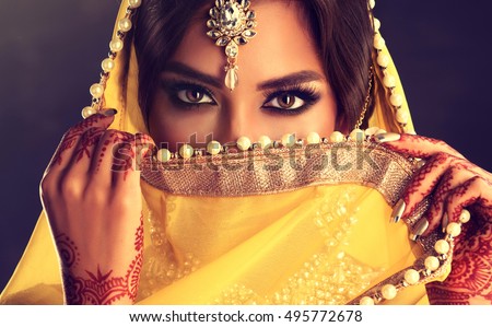 Beautiful indian girl . Young hindu woman model  with tatoo mehndi  and kundan jewelry . Traditional Indian costume yellow saree . Indian or Muslim woman covers her face.