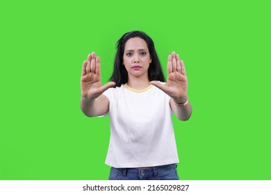 Beautiful Indian Girl Or Young South Asian Woman Making Stop Hand Gesture Isolated Over Green Studio. Stay Away, Go, Don't, Confident Woman Saying No.