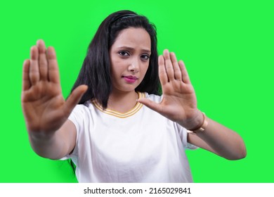 Beautiful Indian Girl Or Young South Asian Woman Making Stop Hand Gesture Isolated Over Green Studio. Stay Away, Go, Don't, Confident Woman Saying No.