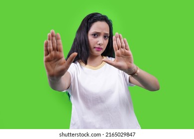 Beautiful Indian Girl Or Young South Asian Woman Making Stop Hand Gesture Isolated Over Green Studio. Stay Away, Go, Don't, Confident Woman Saying No.