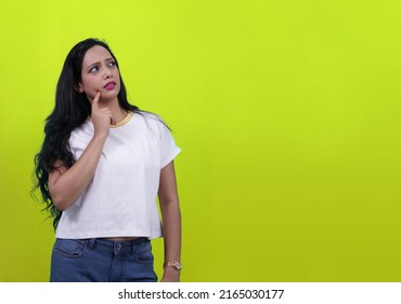 Beautiful Indian girl or Young south Asian woman thinking something deep with finger on face and looking away in right with copy space Isolated in parrot green yellow background.