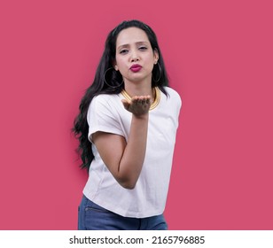 Beautiful Indian girl or Young south Asian woman wearing casual white t shirt looking at the camera blowing kiss with hand on air being lovely and sexy isolated over pink background. love expression