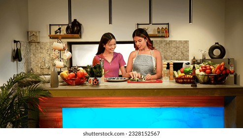 Beautiful Indian two female couple standing in kitchen cutting cucumber on chopping board prepare healthy vegetarian salad. Happy teenage girl feed fresh vegetable slice to woman talk enjoy together - Powered by Shutterstock