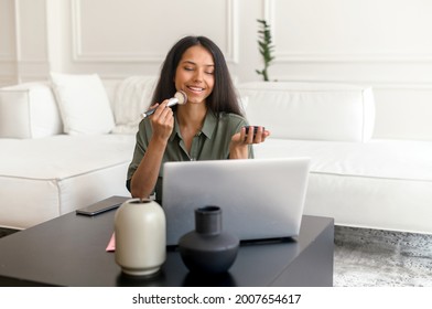 Beautiful Indian Woman Applying Powder With Brush And Watching Makeup Tutorials On Laptop, Charming Smiling Mixed Race Girl Learning To Do Makeup By Herself With Online Tutor