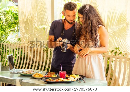 beautiful indian woman and arabian man photographing dishes in summer tropical cafe on camera