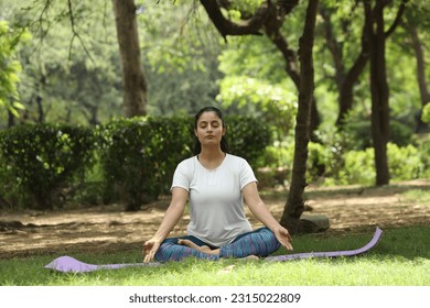 Beautiful indian woman doing breathing yoga exercise in the summer park, Asian female meditation pose, healthcare. copy space - Powered by Shutterstock