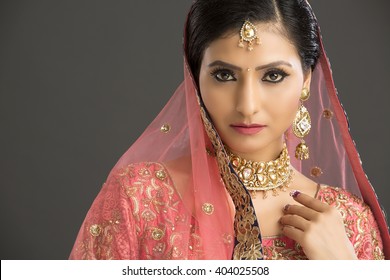 Beautiful Indian woman in glamorous outfit and jewelry with makeup in dark background.