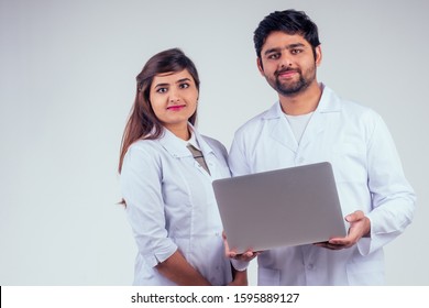 beautiful indian woman and handsome turkey man wearing white blazer coat holding laptop and looking at camera in studio background