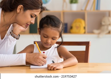 Beautiful Indian woman helping her daughter with homework