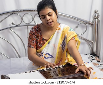 A beautiful Indian woman in saree singing and playing harmonium on white background