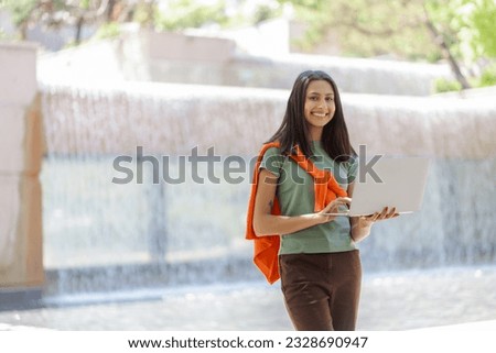 Beautiful Indian woman using digital tablet looking at camera, copy space outdoors. Cute female student, technology concept