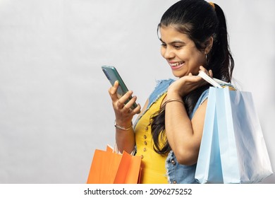 A Beautiful Indian Woman In Yellow Dress With Shopping Bags Looking At Her Smart Phone On White Background