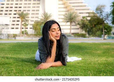 Beautiful Indian Young Woman With Dark Hair And Closed Eyes Lay Down On The Grass In The Park, Concept Of Me Time And Connection With Nature