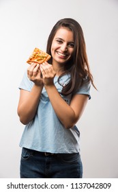 Beautiful Indian/asian young girl eating a slice of pizza standing isolated over white background