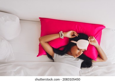 Beautiful Indonesian Girl Lying On A Bright Pink Pillow With A Silk Pillowcase And A Sleep Mask. View From Above
