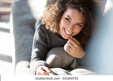 Beautiful Infectious Smile Of A Woman Reading Some Magazine Or Catalogue Relaxed On A Sofa In Her Large And Sunny Living Room