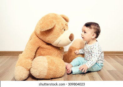 Beautiful innocent newborn speaking with his best friend, teddy bear. Adorable baby playing, having fun with his bear toy. Little sweet kid talking and listening his toy