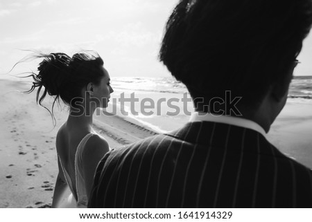 beautiful international wedding couple looking at the sea holding hand, black and white photo