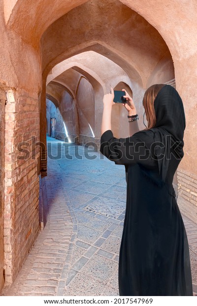 Beautiful Iranian girl wearing\
abaya with taking selfie - Narrow street of old adobe Yazd city -\
IRAN