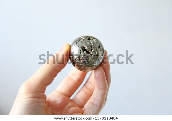 Beautiful iron\
ball in the hand of natural pyrite. On a white background. Golden\
and golden ball or pyrite sphere. Natural stones. Minimalism. The\
shadow of the\
subject.