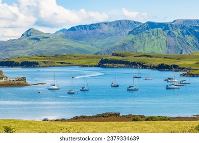 The beautiful Isle of Canna, Inner Hebrides in Summer with yachts and a catamaran in the bay and a RIB speeding towards the harbour with the Isle of Rum in the background.  Horizontal.  Copy space