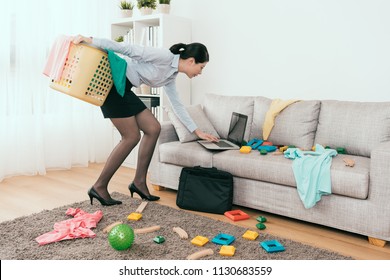 Beautiful Japanese Businesswoman Is Using Notebook Reply The E-mail And Cleaning Up The Mess Toys And Clothes At Home.