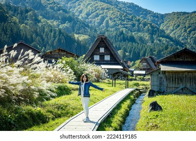 Beautiful Japanese girl with a background of Shirakawago village during autumn with a triangle house, rice field, and pine mountain.