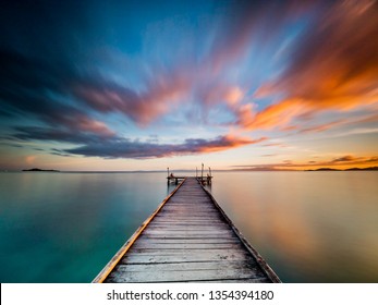 Beautiful jetty sunset long exposure. Minimal shot of a jetty/pier in the centre of the frame stretching out to the ocean. Silky smooth water and streaky sky with orange, purple, pink and blue tones