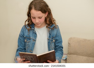 Beautiful Jewish Caucasian Girl Reads Passover Haggadah During Passover Seder In Home. Jewish Family Celebrating Passover. Young Teenager Child Reading Book.