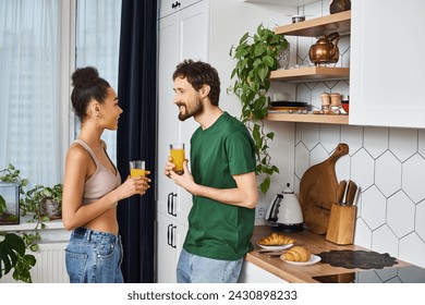 beautiful joyous diverse couple in homewear drinking fresh orange juice and smiling happily - Powered by Shutterstock