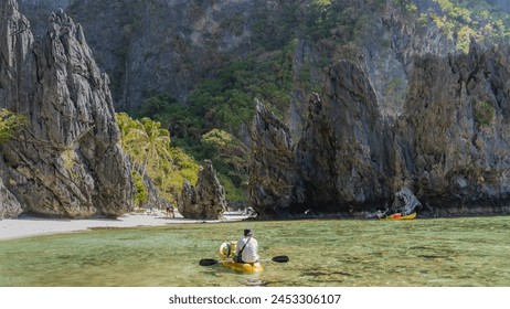 Beautiful karst rocks surround the emerald lagoon. Canoes float in clearwater. People walk along the sandy beach. Green vegetation on steep cliffs. Philippines. Palawan. Bacuit bay. El Nido.  - Powered by Shutterstock