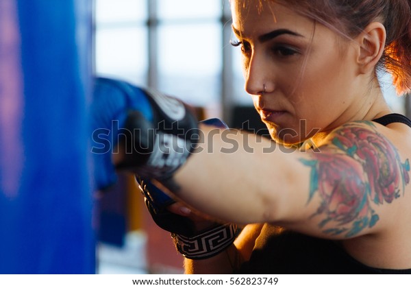 Beautiful Kickboxing woman training punching bag in\
fitness studio fierce strength fit body kickboxer series. Sexy\
fighter girl punching actively. Aggressive and ready to fight.\
Young boxer woman