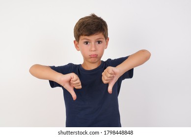Beautiful Kid Boy Wearing Casual T-shirt Standing Over Isolated White Background Being Upset Holding Two Thumbs Down. Dislike Concept. 