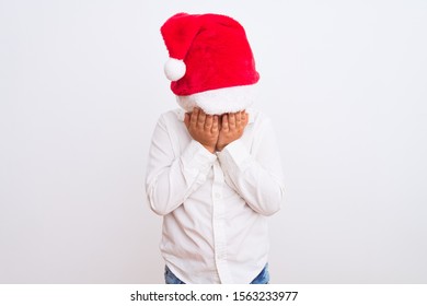 Beautiful Kid Boy Wearing Christmas Santa Hat Standing Over Isolated White Background With Sad Expression Covering Face With Hands While Crying. Depression Concept.