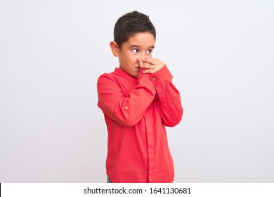 Beautiful Kid Boy Wearing Elegant Red Shirt Standing Over Isolated White Background Smelling Something Stinky And Disgusting, Intolerable Smell, Holding Breath With Fingers On Nose. Bad Smells Concept