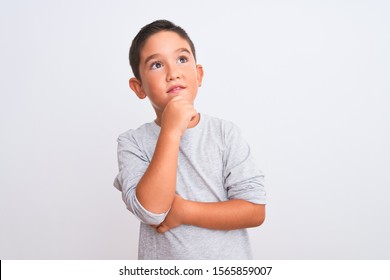 Beautiful Kid Boy Wearing Grey Casual T-shirt Standing Over Isolated White Background With Hand On Chin Thinking About Question, Pensive Expression. Smiling With Thoughtful Face. Doubt Concept.