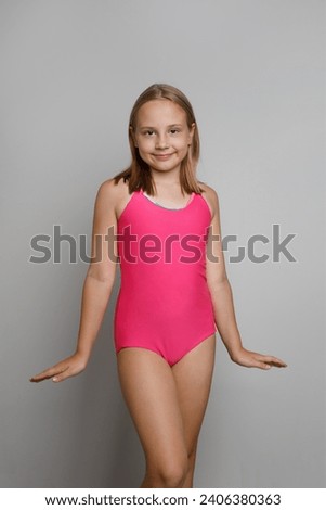 Beautiful kid child girl in pink swimsuit posing on light gray studio wall background. Travel, sport, swimming activities and vacations concept