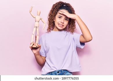 Beautiful kid girl with curly hair holding small wooden manikin stressed and frustrated with hand on head, surprised and angry face  - Powered by Shutterstock