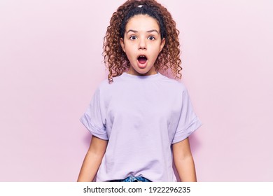 Beautiful Kid Girl With Curly Hair Wearing Casual Clothes Scared And Amazed With Open Mouth For Surprise, Disbelief Face 