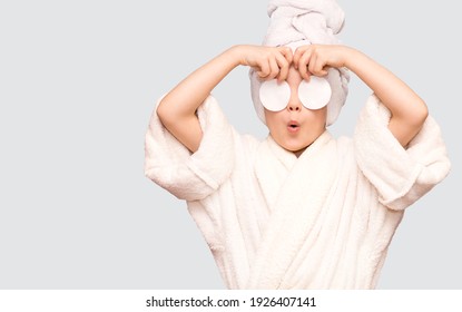 Beautiful Kid Girl With Surprised Face And Towel On Head Hold Cotton Pad Disk Cleansing Face Skin With Cleanser Isolated On White Background. Happy Girl Remove Makeup Look At Camera Enjoy Healthy