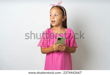 beautiful kid girl wearing pink dress holding a smartphone and looking sideways at blank copyspace.