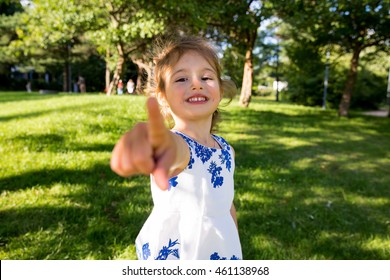 Beautiful Kid Taking Selfie In Green Summer Park, Laughing, Having Fun. Warm Sunny Weather, Healthy Child, Happiness, Freedom, Emotions. Cute Girl Reaching Finger To Camera, Pointing.