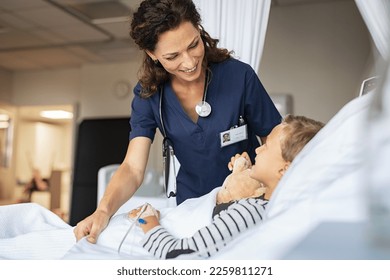 Beautiful kind female nurse taking care of little boy hospitalized in bed. Happy woman nurse tuck the covers back to the young child patient lying on hospital bed. Medical worker with kid patient. - Powered by Shutterstock