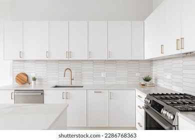 A beautiful kitchen detail with white cabinets, a gold faucet, white marble countertops, and a brown picket ceramic tile backsplash.