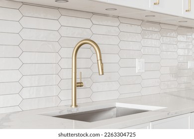 A beautiful kitchen faucet detail with white cabinets, a gold faucet, white marble countertops, and a brown picket ceramic tile backsplash. - Shutterstock ID 2263304725