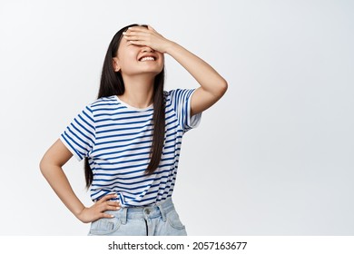 Beautiful Korean Girl Covering Her Eyes For Surprise, Smiling From Anticiaption, Waiting For Something Blindfolded, Standing Over White Background