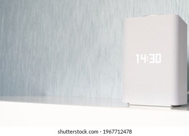 A beautiful, laconic white speaker in a minimalist style stands on a white table in a room with blue-gray walls.