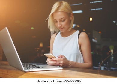 Beautiful lady chatting on smart phone while sitting at the table with laptop computer in cafe bar interior, pretty European woman using cell telephone while relaxing after work on portable net-book 